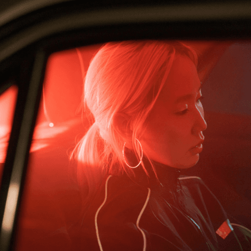 Young woman sitting in a car under red lighting, symbolizing modern consumer journeys, mobility trends, and audience context for marketing.